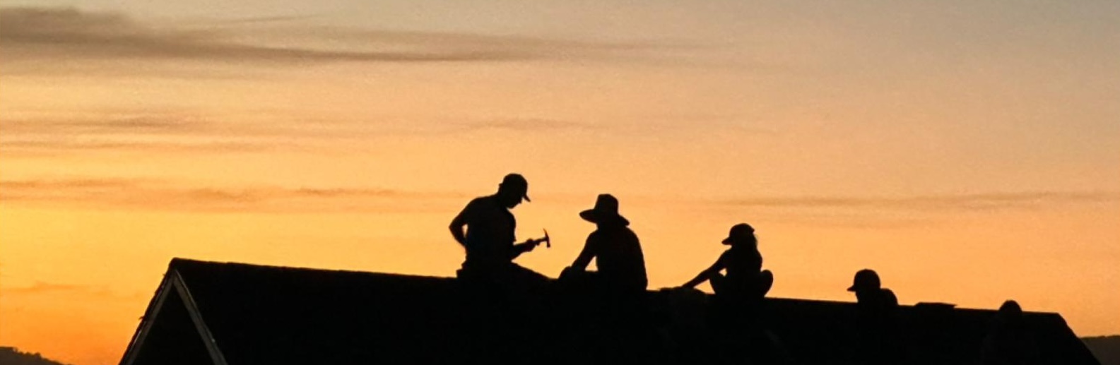 Silhouettes of people on top of the roof of a house during sunset.